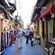 Un estrecho pasaje bordeado por pequeñas tiendas que venden bufandas, frutas y otros productos